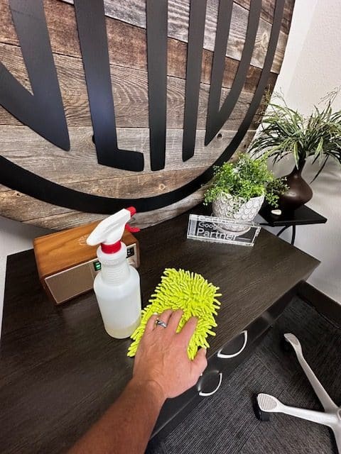Photo of a mans arm cleaning a business entryway table with a spray bottle and rag.